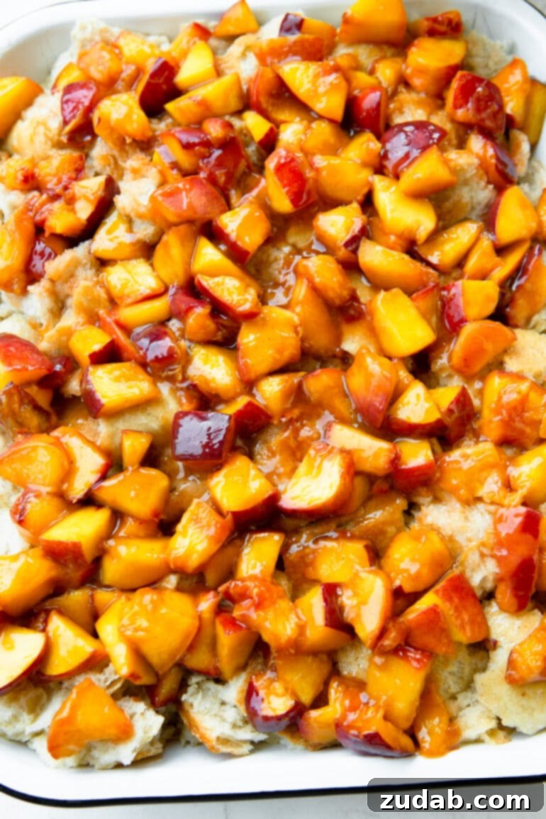 Delicious Peach Cobbler French Toast 8 A photo of juicy diced peaches layered on top of torn chunks of white bread in a baking dish, ready for the next step.