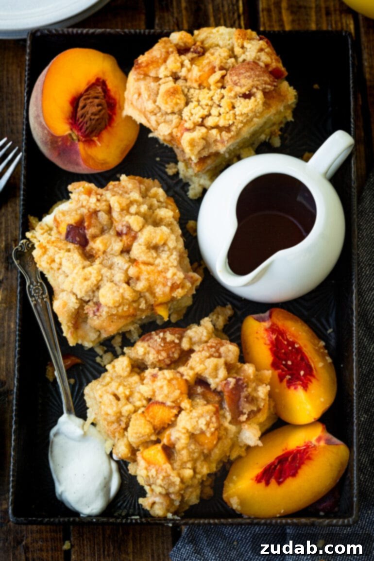 Delicious Peach Cobbler French Toast 10 A photo of several servings of baked peach cobbler french toast casserole on a serving tray, surrounded by fresh peach slices and a carafe of syrup, ready for a gathering.
