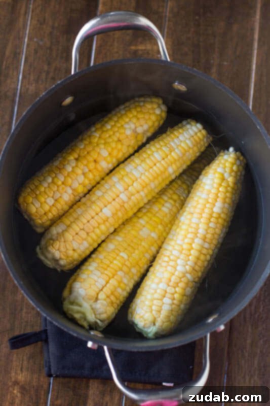 Blanching corn on the cob for optimal flavor preservation. Several ears of fresh corn being blanched in a large pot of boiling water, steam rising.