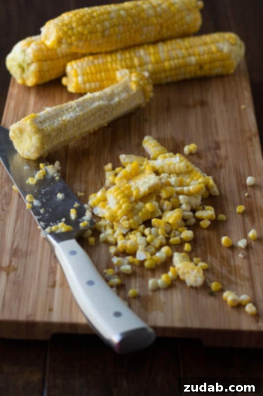 Efficiently slicing fresh corn kernels off the cob for freezing. A cutting board with a bare corn cob and a pile of freshly sliced corn kernels, ready for packaging.