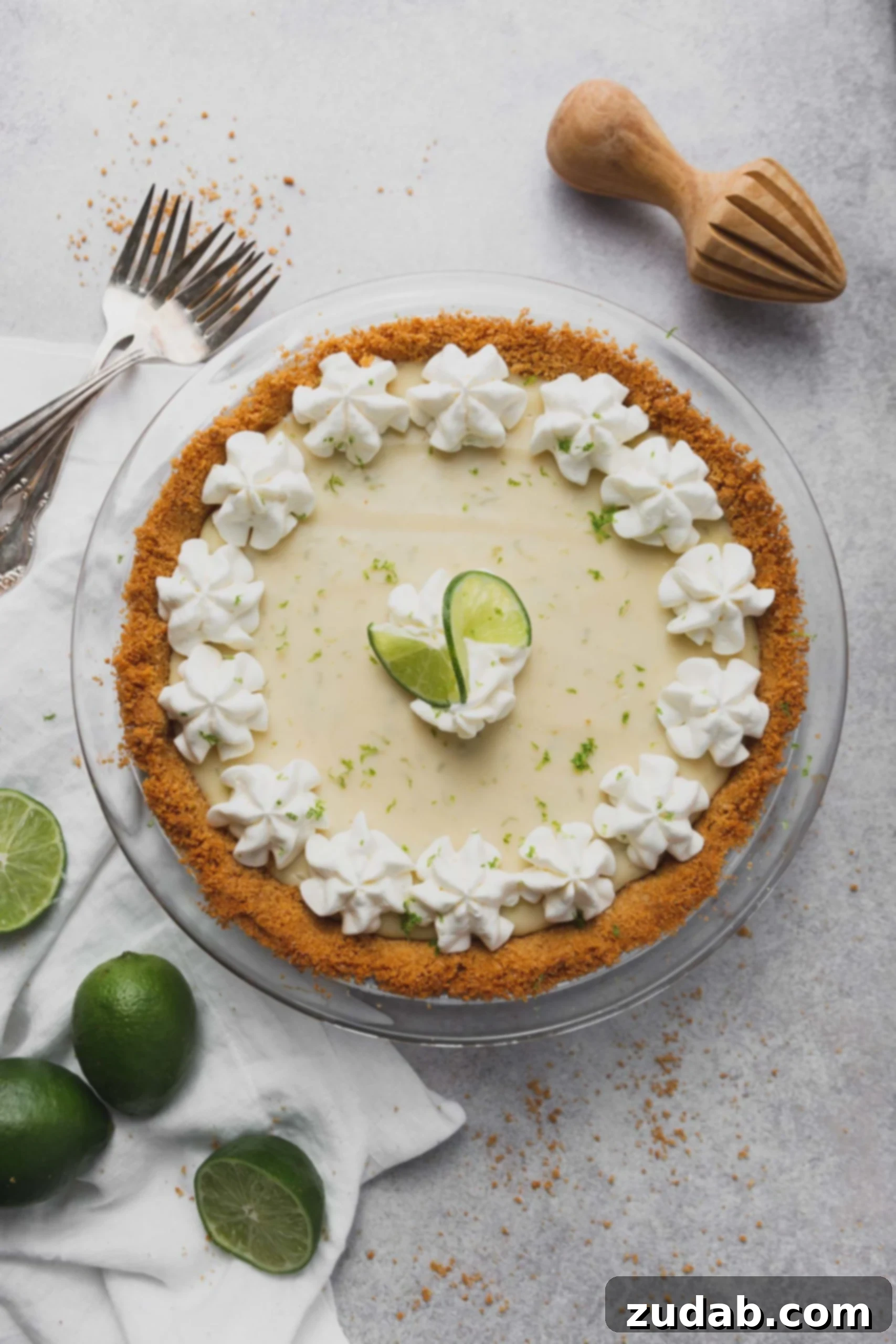 Key Lime Pie Recipe A key lime pie in a graham cracker crust. Dollops of whipped cream are around the edge of the pie and two slices of lime are in the middle. Limes and forks are beside the pie.