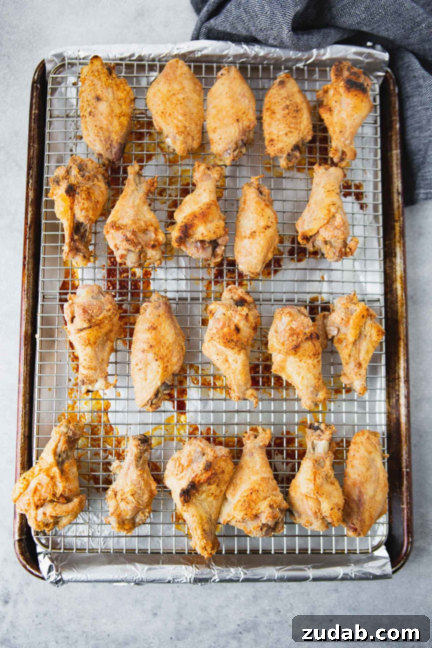 Baked Chicken Wings on Cooling Rack Golden brown, perfectly baked chicken wings arranged neatly on a wire cooling rack set inside a baking sheet. The crispiness of the skin is evident, indicating they are ready for saucing.