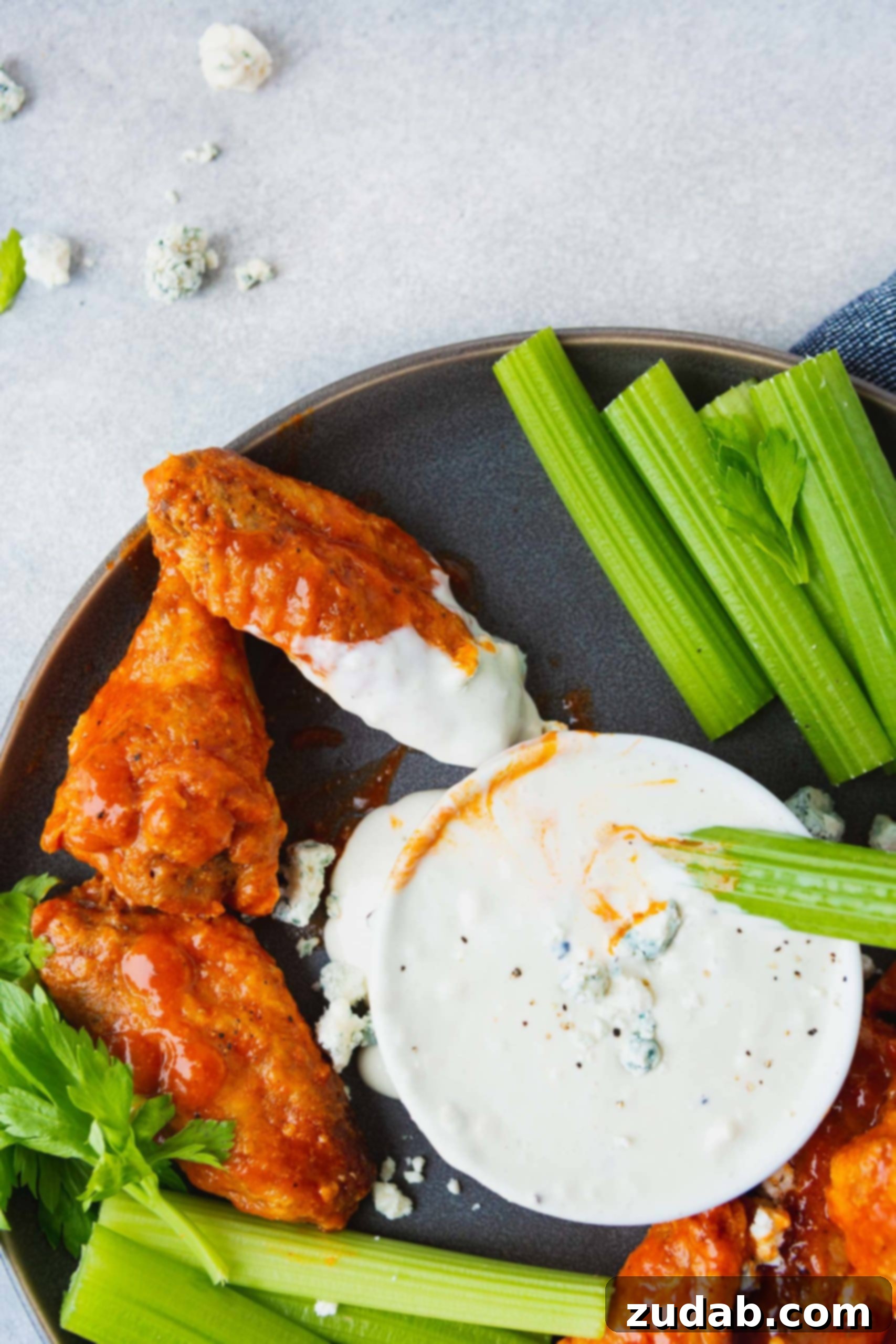 Buffalo Wings with Blue Cheese Dip and Celery A charcoal platter filled with buffalo wings and celery. A cup of blue cheese dressing sits in the middle, with one wing and one stick of celery dipped into it, emphasizing the classic pairing.
