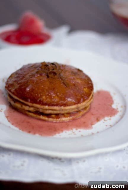 Dark chocolate pancakes generously covered with vibrant strawberry syrup, a delightful combination for a sweet breakfast.