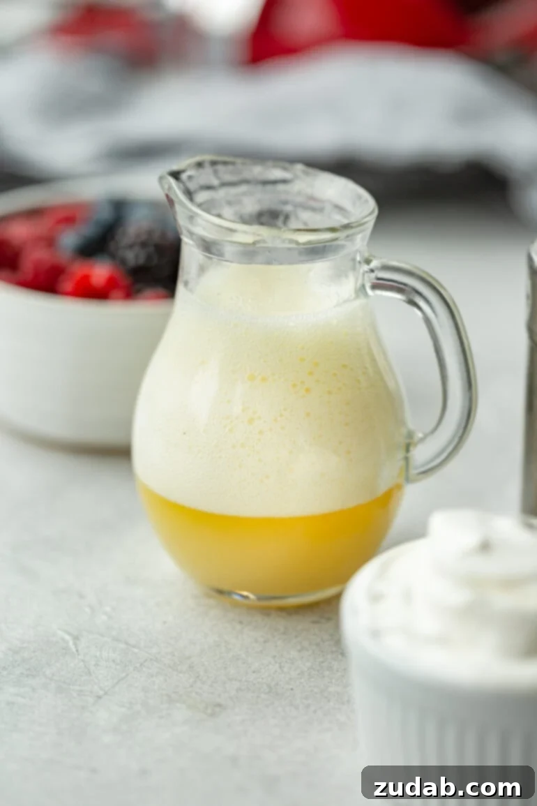 A close-up photo of a glass pitcher showing the significant amount of white foam that forms on top of golden buttermilk syrup immediately after baking soda is added, demonstrating a crucial step in the recipe.