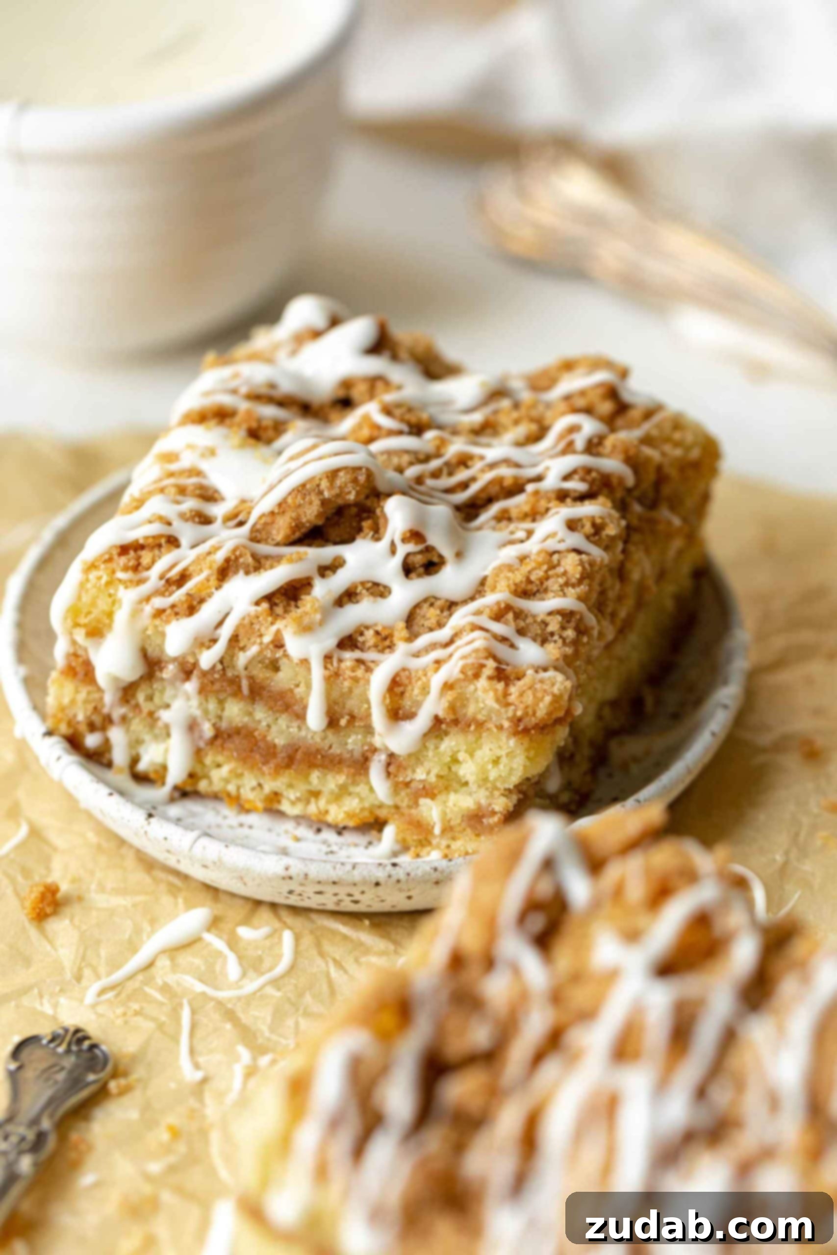 The Coffee Cake That Makes Starbucks Seem Basic 2 a photo of a piece of coffee cake topped with icing drizzles on a small saucer with another piece in the foreground.