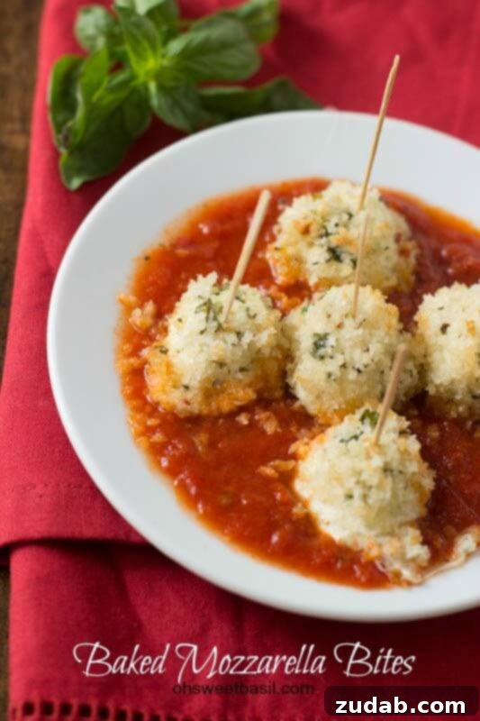 The Best Baked Mozzarella Bites Recipe Three baked mozzarella bites on a white plate, ready to be dipped in a side of marinara sauce.