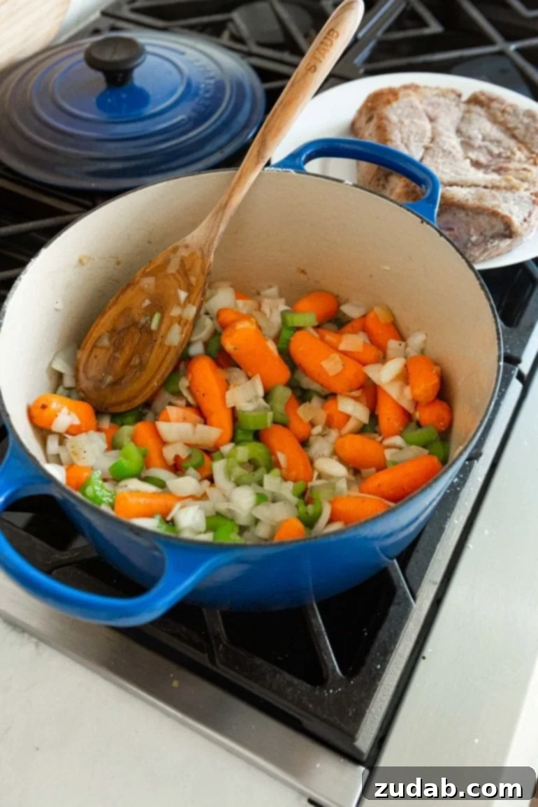 My Best-Ever Pot Roast and Gravy 2 A photo of a large dutch oven will of whole baby carrots, diced onions and celery with a wooden spoon in the pot.