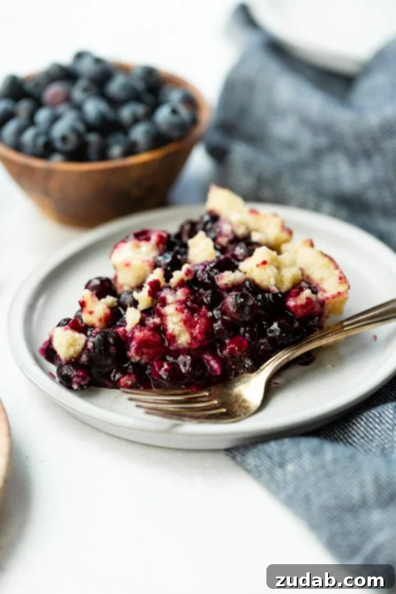 Wild Blueberry Shortbread Bliss 3 A photo of a slice of wild blueberry pie sitting on a small dessert plate with a silver fork next to it, showing the vibrant filling and crumbly topping.