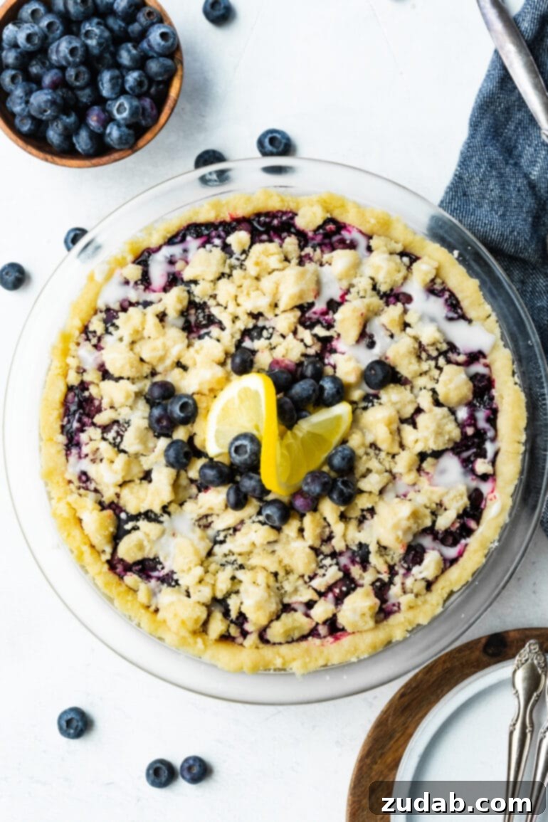Wild Blueberry Shortbread Bliss 5 A photo of a whole wild blueberry pie topped with a golden streusel and garnished with a slice of fresh lemon, ready for serving.