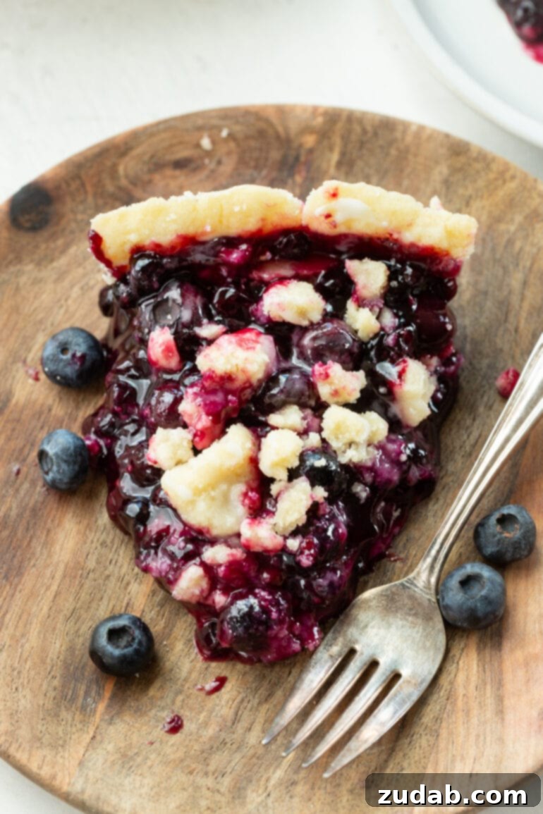 Wild Blueberry Shortbread Bliss 7 A photo of a slice of wild blueberry pie with golden streusel topping and a fork sitting right next to it, inviting a bite.