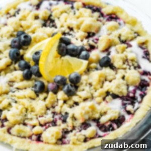 A photo of a whole baked wild blueberry pie in a shortbread crust with a streusel topping and a vanilla glaze.