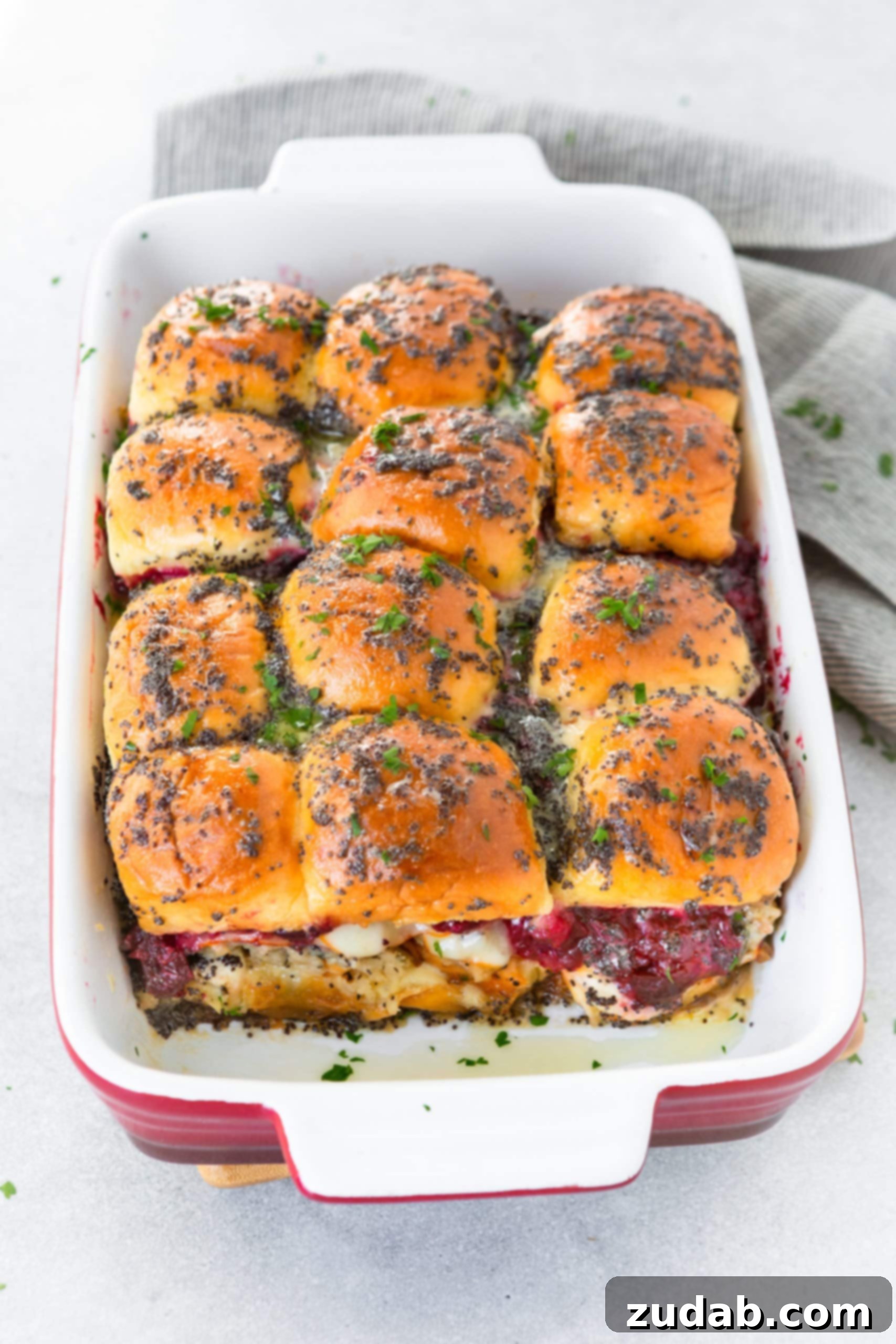 Baked Turkey Sliders with Poppy Seed Dressing A mouth-watering photo of a baking dish filled with golden-brown turkey sliders, glistening with poppy seed dressing, with cheese and cranberry sauce bubbling and oozing out, promising a delectable feast.