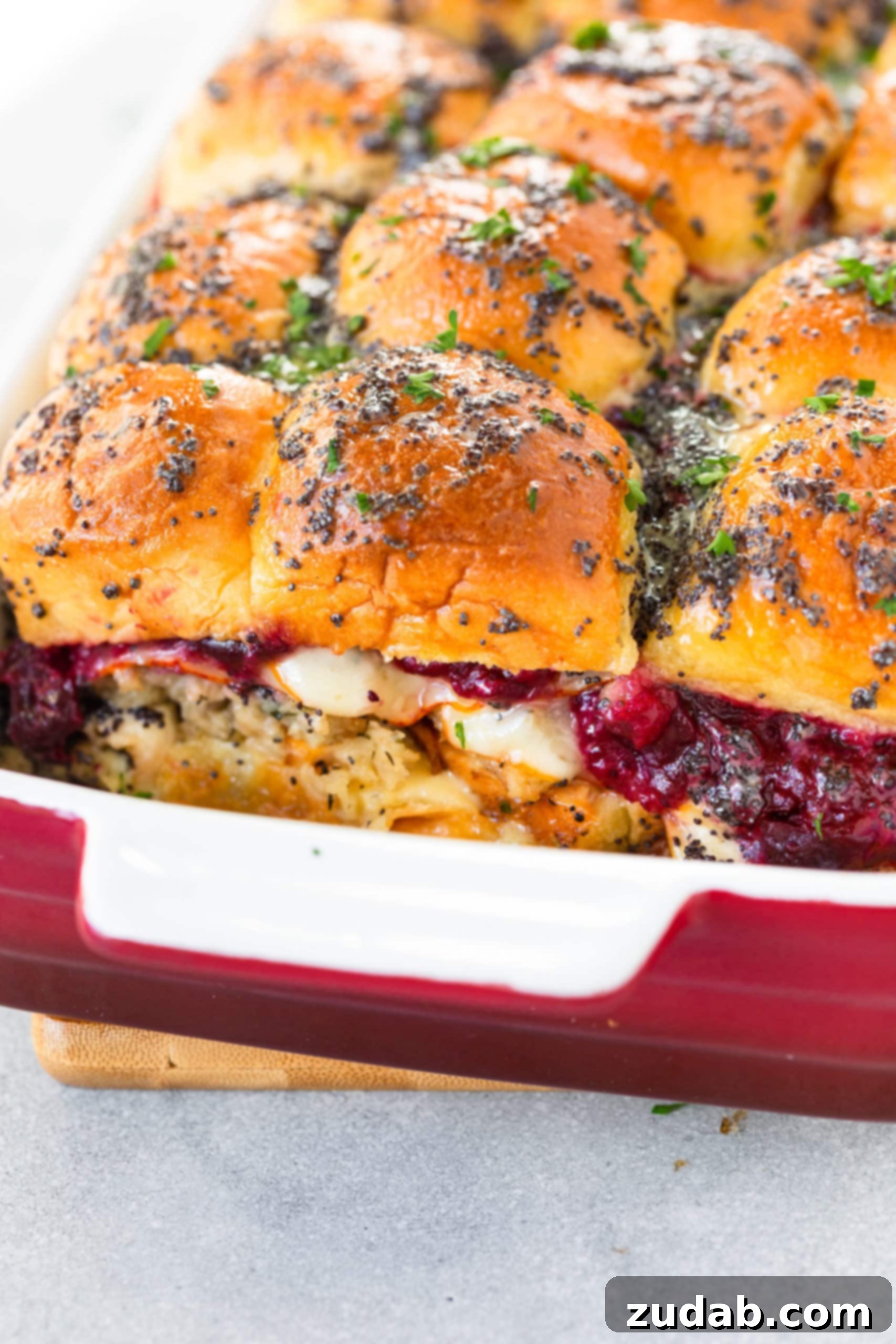 Gourmet Turkey and Cranberry Sliders A stunning close-up photo of several baked turkey sliders nestled in a 9x13 baking dish, with luscious cranberry sauce and melted white cheddar cheese gracefully dripping out, highlighting the irresistible combination of flavors.