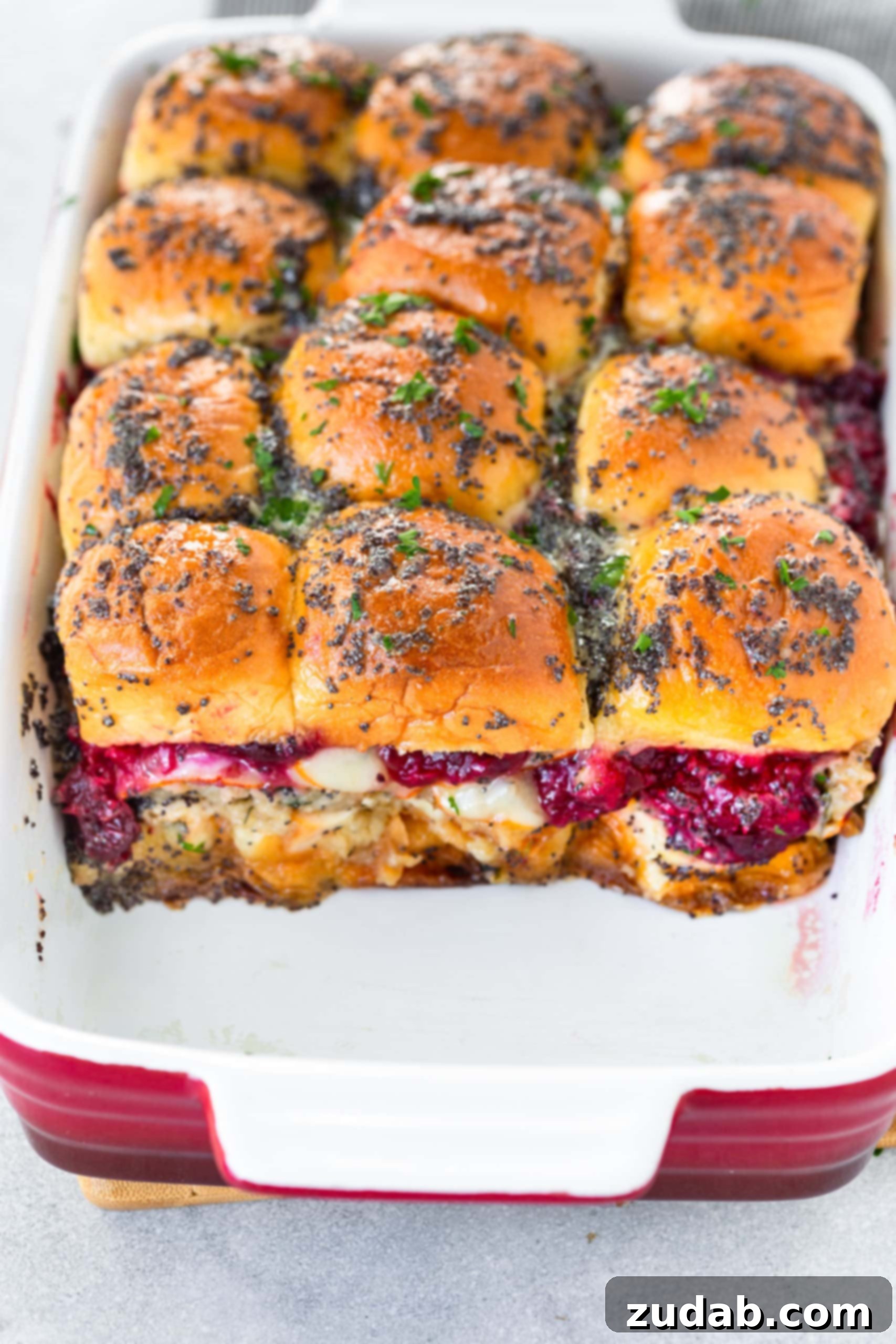 The Perfect Baked Turkey Sliders A photo showcasing a 9x13 baking dish filled with nine perfectly baked turkey sliders. The first row has been removed, revealing the delightful layers of tender turkey, irresistibly melted cheese, and sweet cranberry sauce spilling out from the sides.
