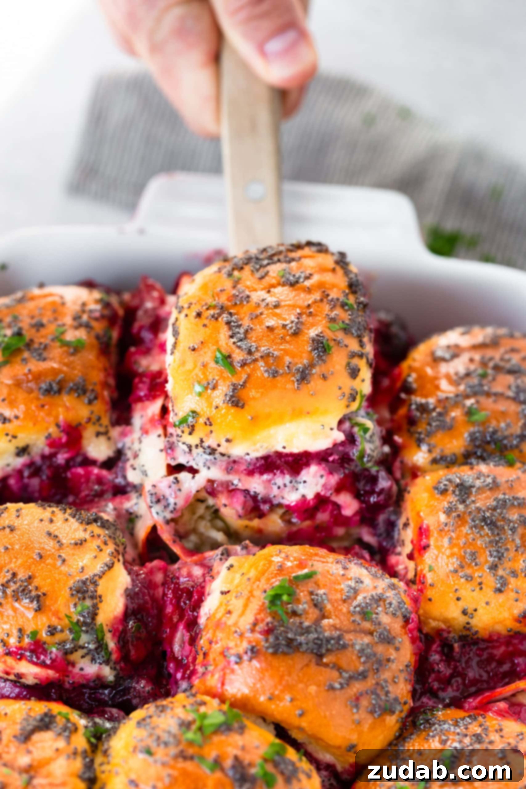Melted Cheese and Cranberry Turkey Slider A captivating photo of a golden-baked turkey slider being carefully lifted from a baking dish full of more irresistible sliders. The close-up reveals luscious cranberry sauce and delightfully melted cheese oozing out, promising pure culinary bliss.