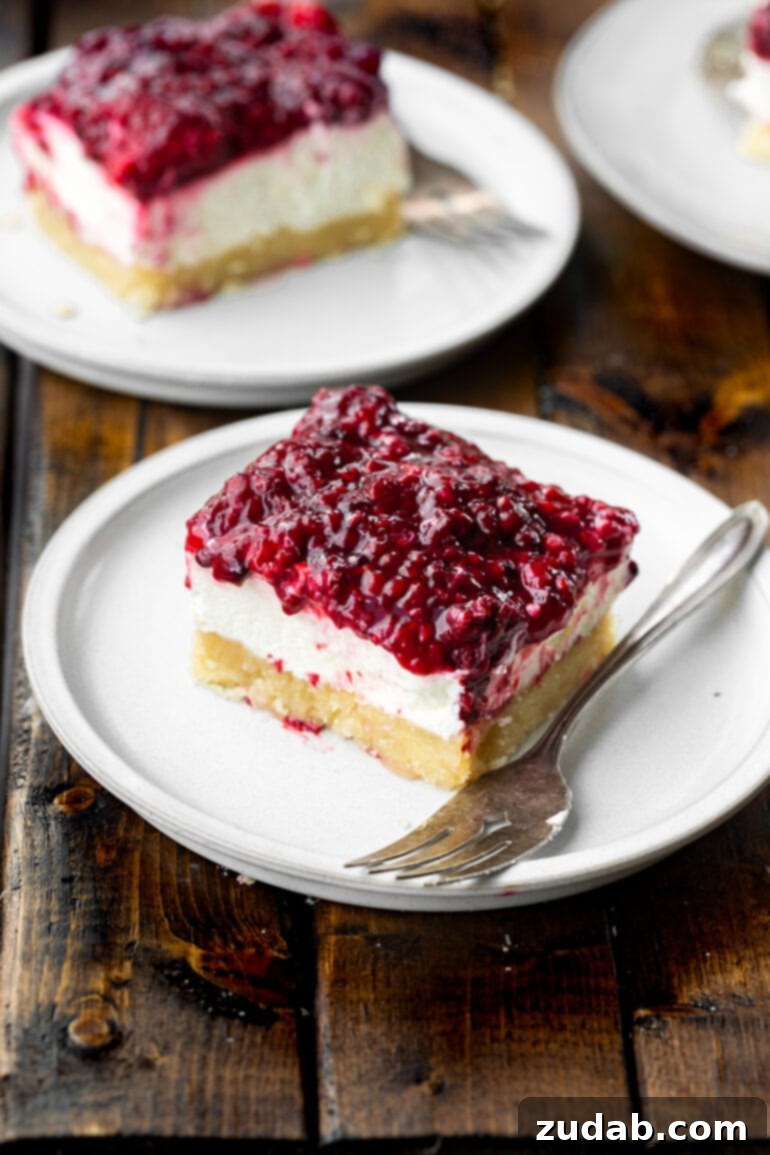 Berry Bliss Cheesecake Bars 7 a photo of a berries and cream cheesecake bar sitting on a small white dessert plate with a fork sitting next to it.