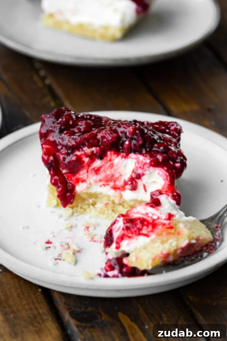 Berry Bliss Cheesecake Bars 8 a photo of a berries and cream cheesecake bar with a fork removing a bite from it and the fork sitting next to the piece.