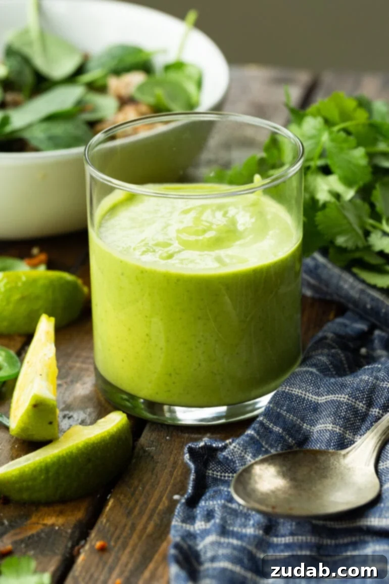 Fresh Creamy Avocado Cilantro Lime Dressing 2 A glass cup filled with bright green avocado cilantro lime dressing, garnished with fresh lime wedges and cilantro leaves. This vibrant dressing is perfect for salads, tacos, and rice bowls.
