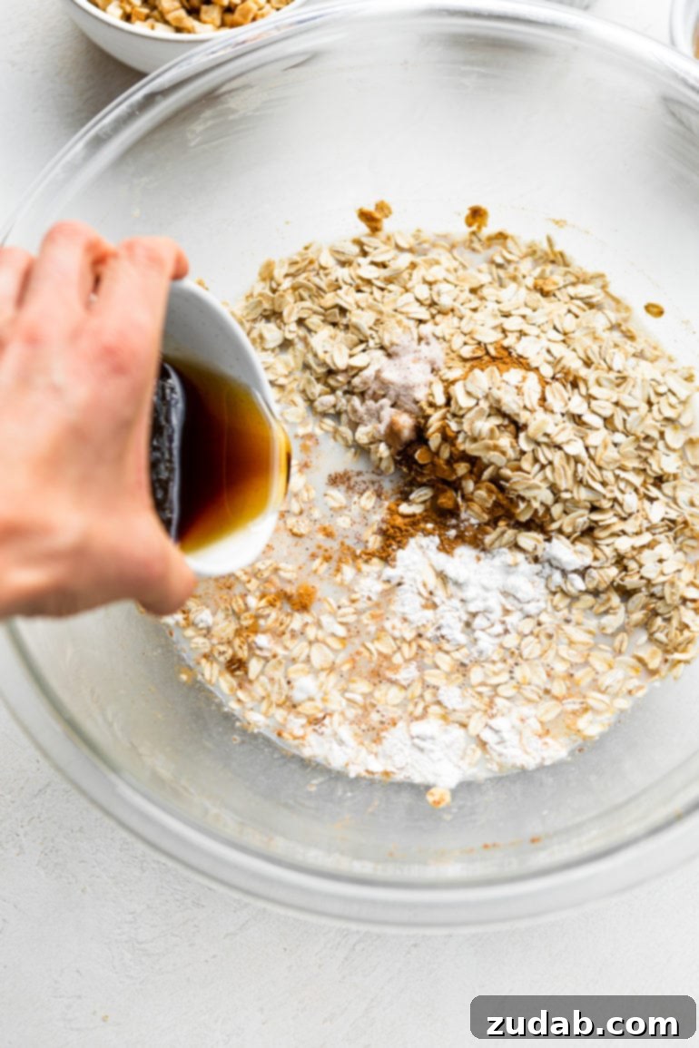 Wholesome Apple Fritter Baked Oats 2 A photo of vanilla extract being poured into a bowl of uncooked oats and milk, illustrating the initial mixing steps of the recipe.