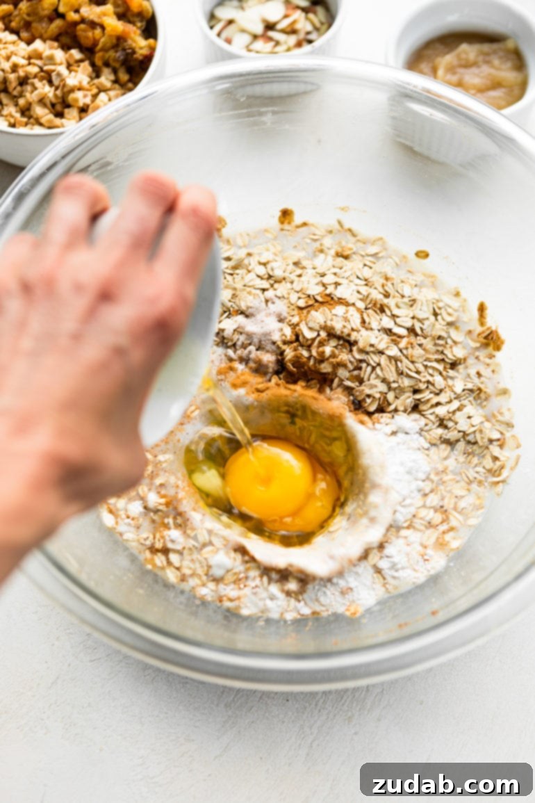 Wholesome Apple Fritter Baked Oats 3 A photo capturing two eggs being gently poured into a glass bowl filled with the base ingredients for healthy apple fritter baked oatmeal, an essential step in the preparation.