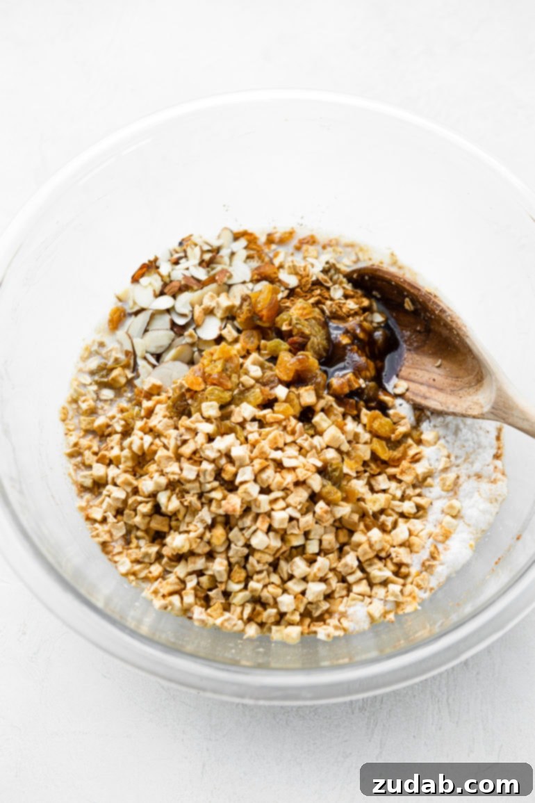 Wholesome Apple Fritter Baked Oats 5 A photo depicting a wooden spoon actively stirring a large glass bowl filled with the combined ingredients for healthy apple fritter baked oatmeal, highlighting the mixing process.