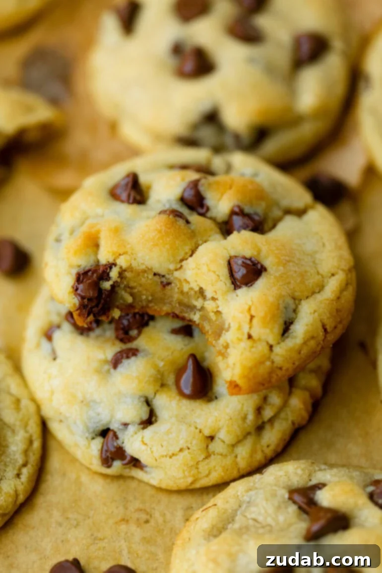 A tantalizing photo of perfectly golden-baked chocolate chip cookies, stacked high on a rustic wooden board, their melted chocolate chips glistening.