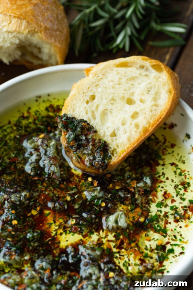 Sizzling Italian Dipping Oil for Crusty Bread 3 a photo of a slice of french bread that has been partially dipped in an herby Italian dipping oil sitting on the side of a bowl of the bread dip.