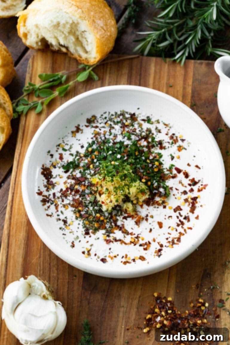 Sizzling Italian Dipping Oil for Crusty Bread 4 a photo of a shallow white bowl full of a mixture of minced fresh herbs, red pepper flakes and minced garlic.