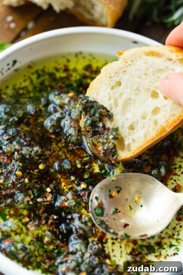 Sizzling Italian Dipping Oil for Crusty Bread 6 a photo of a slice of french bread being dipped into a shallow bowl full of Italian dipping oil.