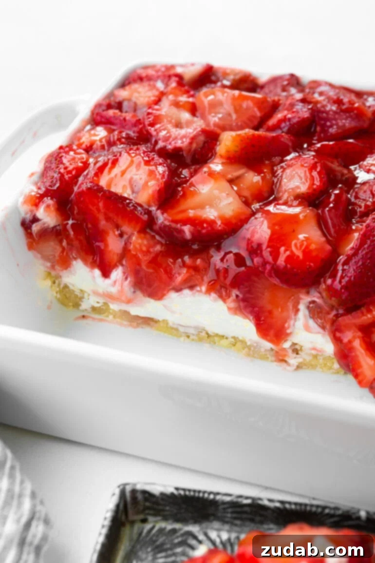 Luscious Strawberry Cheesecake Squares 3 A close-up photo of a pan of creamy strawberry cheesecake bars with several pieces already removed, showcasing the distinct layers of the flaky crust, thick cream cheese filling, and generous strawberry topping from the side view.