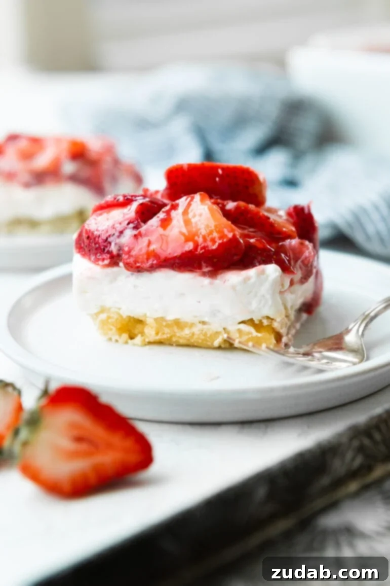 Luscious Strawberry Cheesecake Squares 5 A beautiful, close-up photograph of a single strawberry cheesecake bar, showcasing its thick, creamy layers and an abundance of bright, juicy red strawberries on top, sitting on a small white plate.