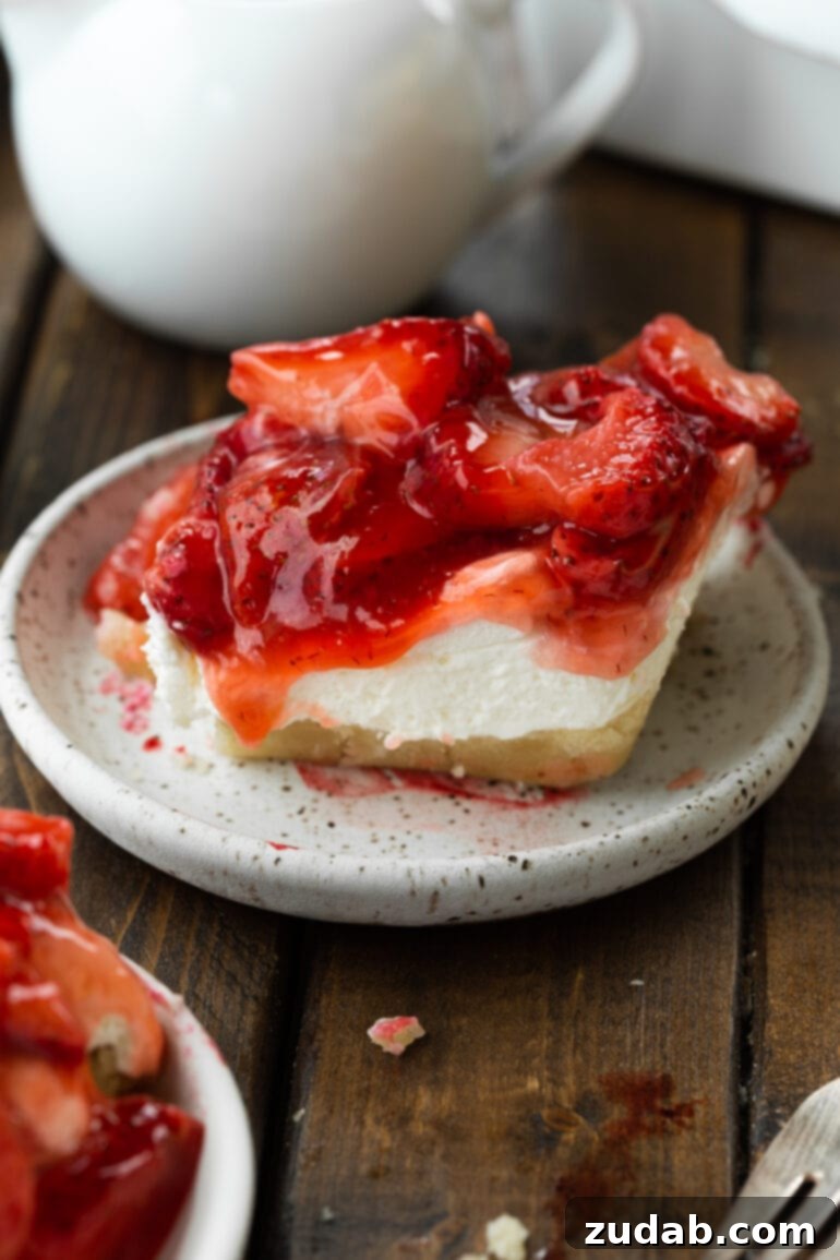 Luscious Strawberry Cheesecake Squares 6 A close-up of a delectable piece of strawberry and cream bar, showing its distinct layers: a thick, golden, flaky crust at the bottom, a creamy white filling, and a generous topping of vibrant, juicy strawberries.