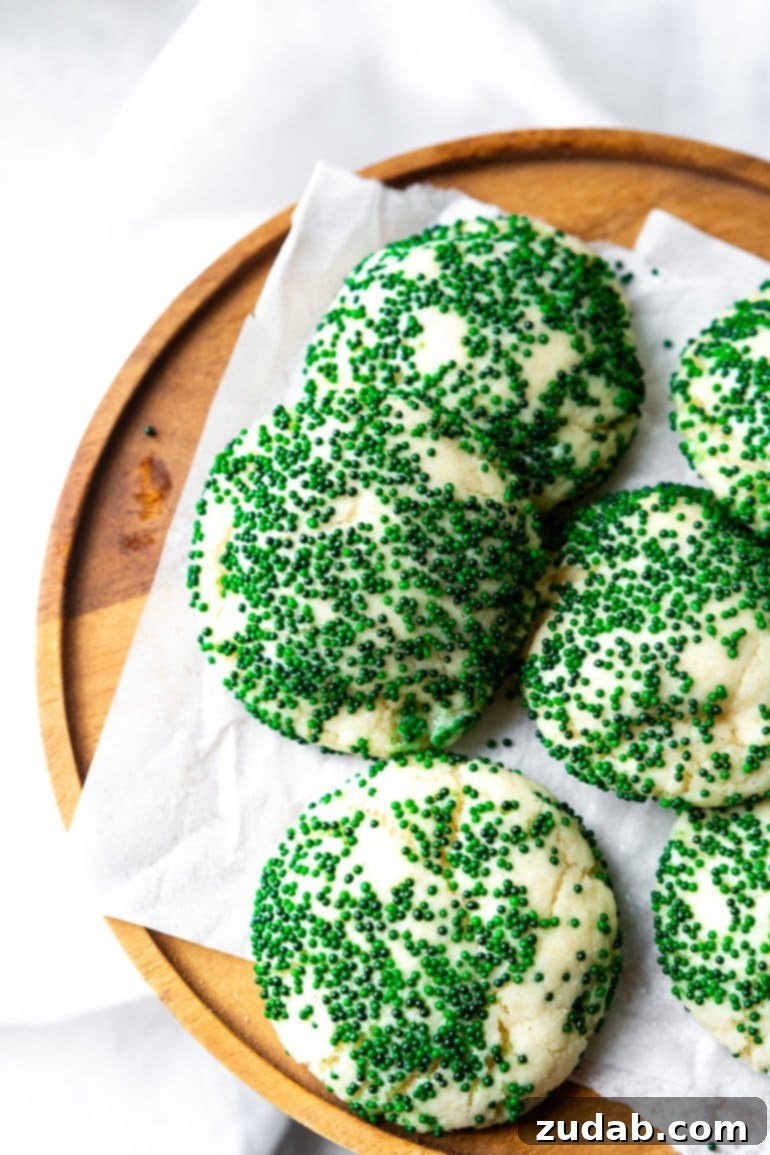 Festive Cookie Collection 7 A photo of several thick and soft sugar cookies artfully arranged on a piece of white parchment paper atop a rustic wooden serving tray. The cookies are generously coated in dark green sprinkles, adding a festive touch.