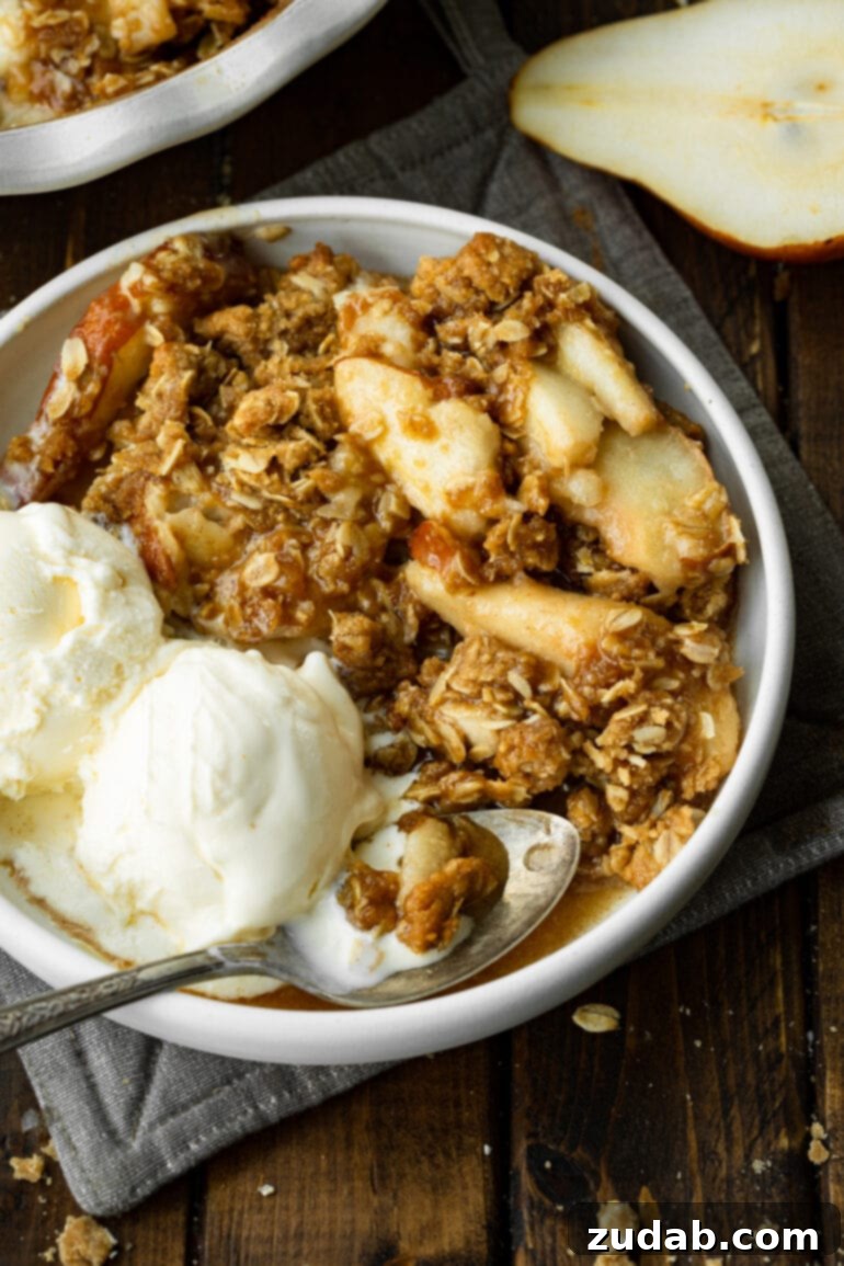 Heavenly Pear Crisp 2 A bowl of pear crisp adorned with two generous scoops of vanilla ice cream, ready to be enjoyed with a spoon.