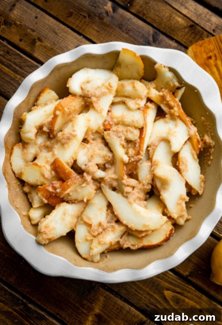 Heavenly Pear Crisp 6 A deep pie dish generously filled with sliced pears, beautifully coated in a butter and cinnamon mixture, ready for baking.