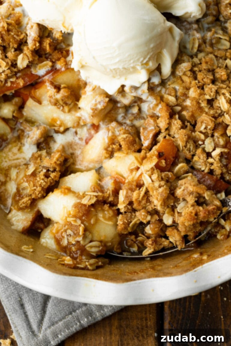Heavenly Pear Crisp 7 A circular baking dish filled with pear crisp, showcasing a golden, perfectly baked oat topping and accompanied by scoops of creamy vanilla ice cream.