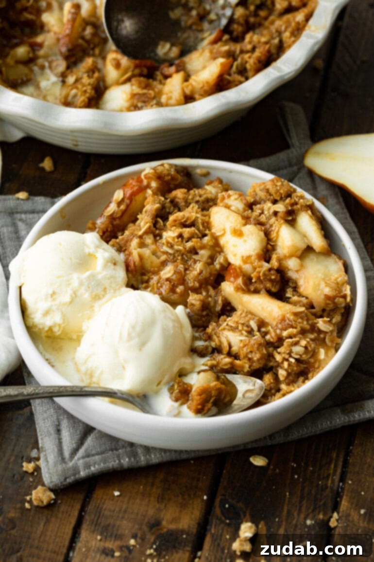 Heavenly Pear Crisp 8 A pristine white bowl showcasing a generous serving of pear crisp, beautifully crowned with two scoops of creamy vanilla ice cream.