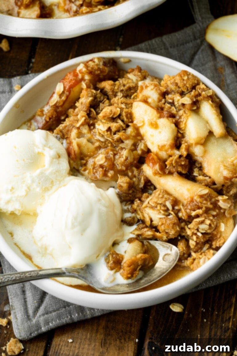 Heavenly Pear Crisp 10 A delightful photo of a bowl featuring juicy, tender baked pears, crowned with a golden oat topping, and flanked by two scoops of luscious vanilla ice cream.