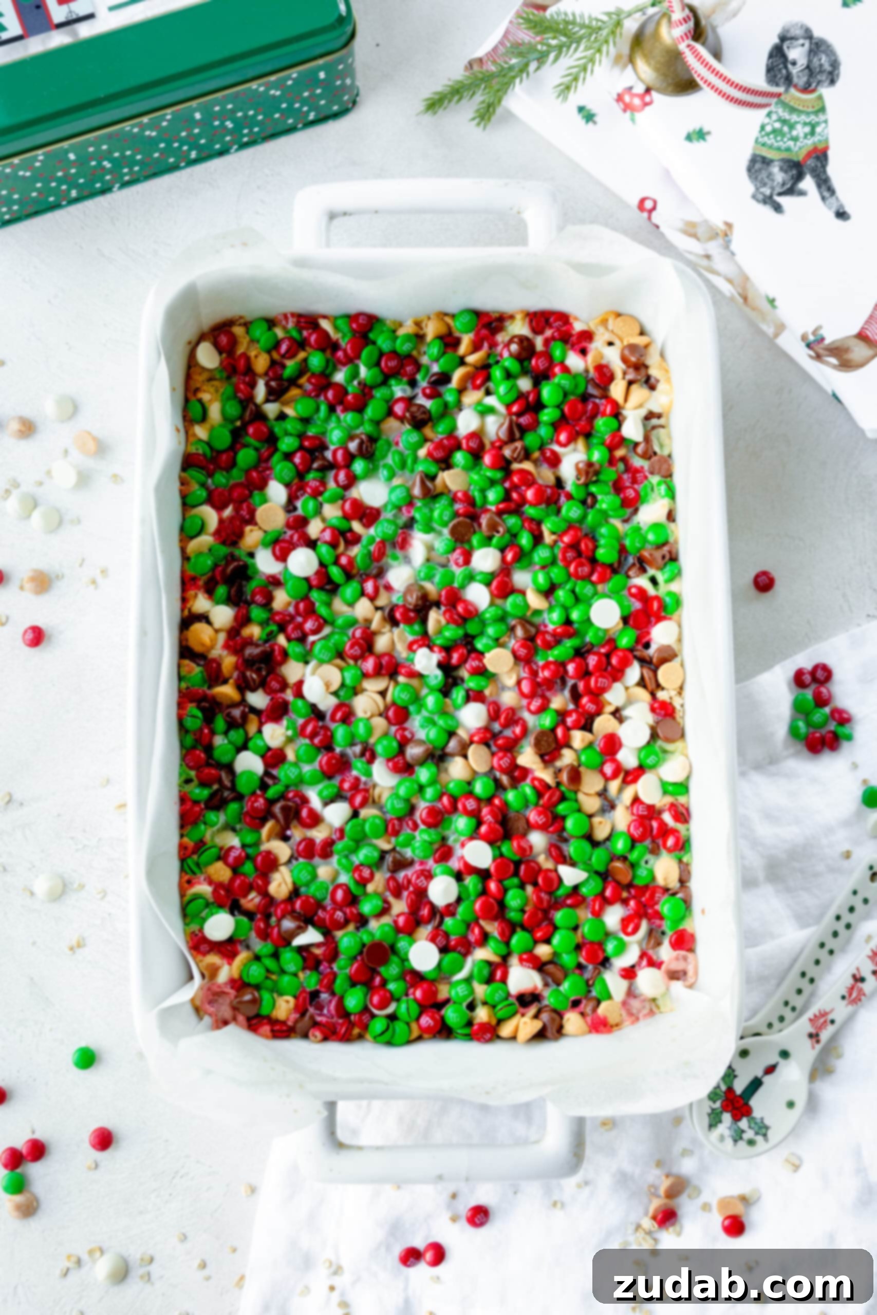 Christmas Magic Cookie Bars A photo of a 9x13 white ceramic baking dish full of colorful magic cookie bars complete with red and green M&M's, white chocolate chips, peanut butter chips, and semi-sweet chocolate chips.