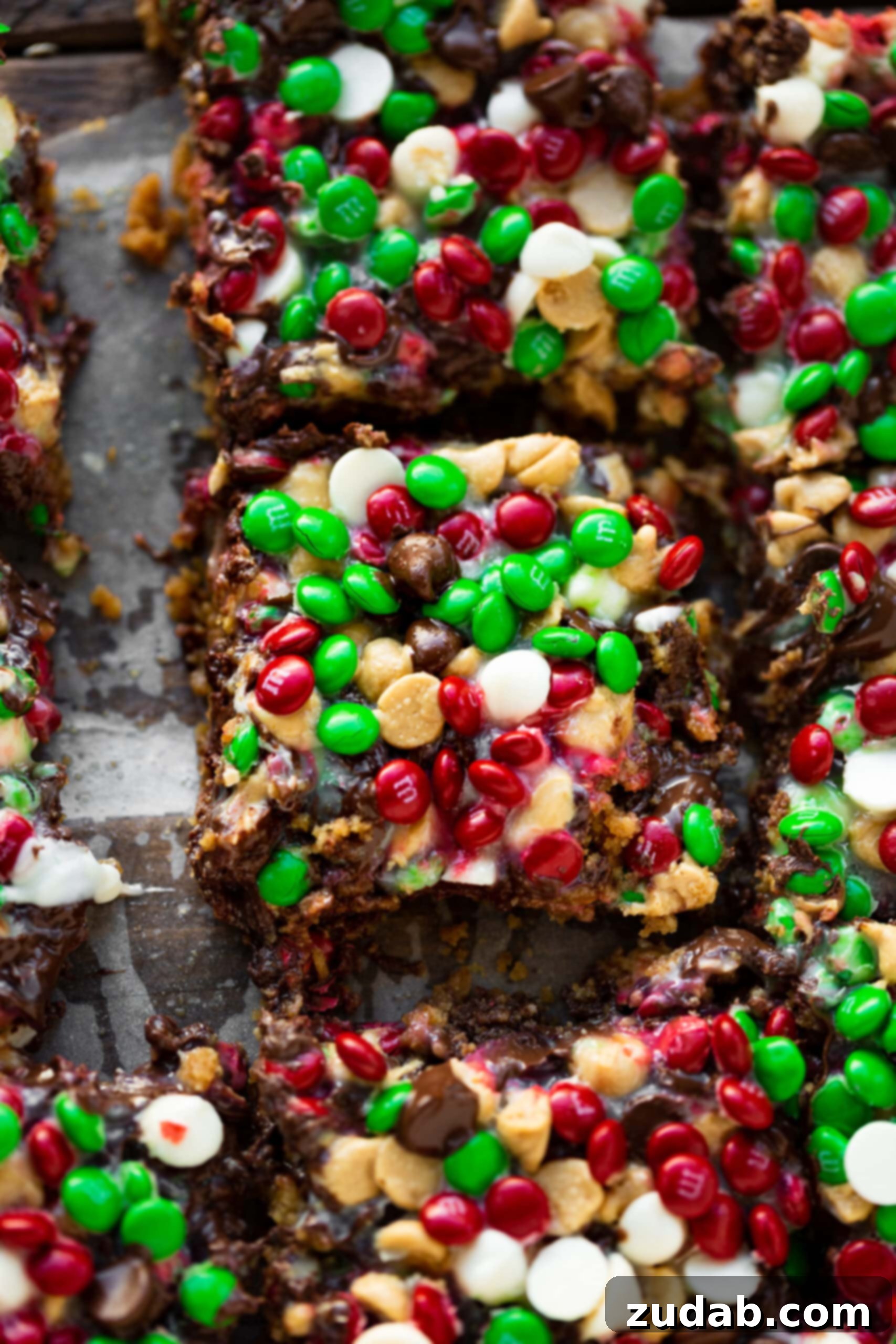 Christmas Magic Cookie Bars A photo of several square pieces of magic cookie bar topped with red and green holiday M&M's, peanut butter chocolate chips, white chocolate chips, and semi-sweet chocolate chips.
