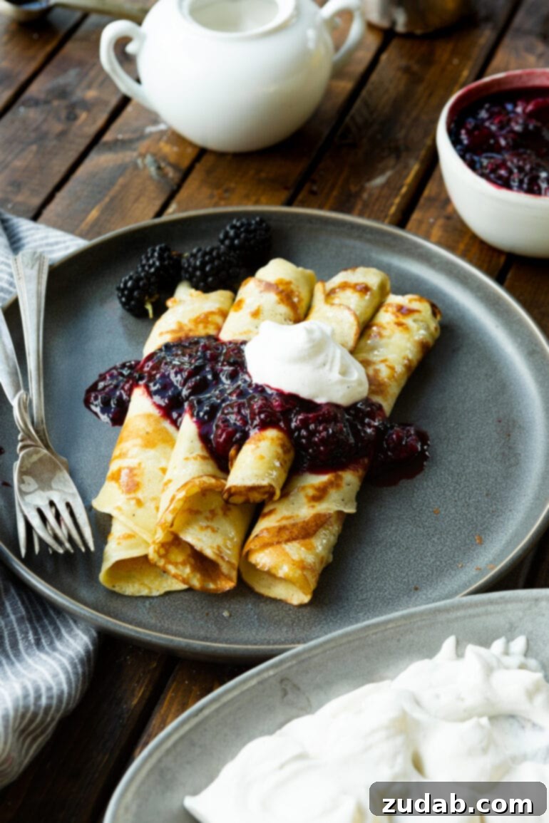 A close-up photograph showcasing five perfectly rolled, golden-brown Finnish pancakes, exquisitely garnished with a vibrant blackberry sauce and a delicate dollop of whipped cream, inviting a delightful taste.