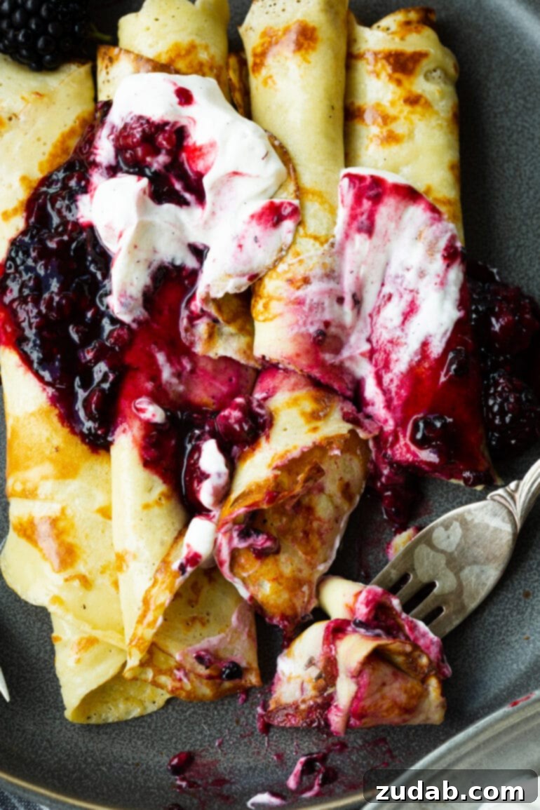 A delectable photo of several rolled Finnish pancakes adorned with plump blackberries and fluffy whipped cream, with a fork poised to cut a perfect bite, emphasizing their irresistible appeal.