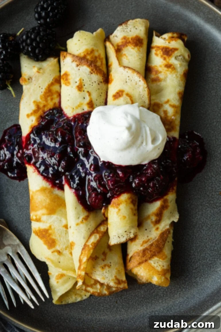 A stunning photo of several golden, pan-fried Finnish pancakes, delicately rolled and beautifully topped with a luscious blackberry sauce and a swirl of whipped cream, inviting a taste of traditional Finnish breakfast.