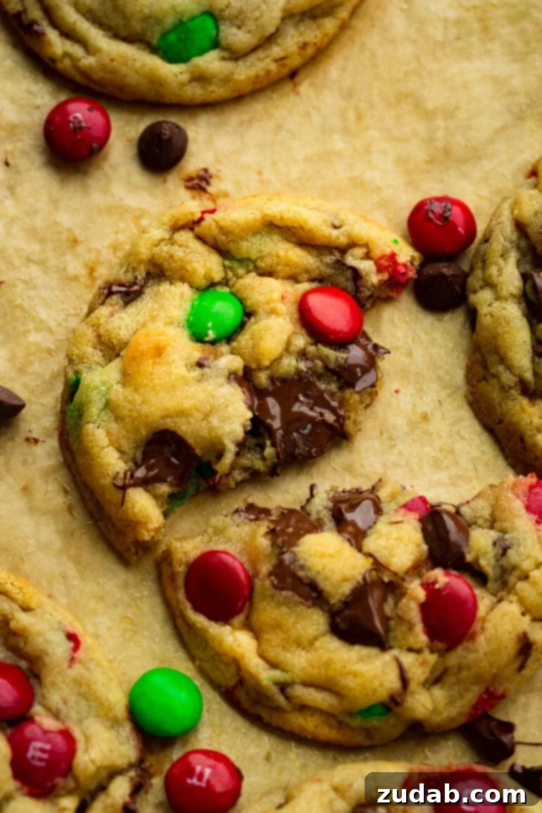 A golden-baked Christmas M&M chocolate chip cookie broken in half, revealing its delightfully gooey and soft center.