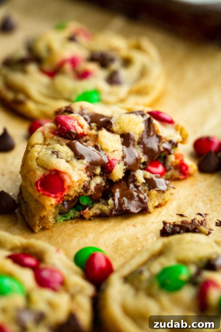 A stack of thick, chewy M&M chocolate chip cookies, broken in half to showcase their delightful, gooey centers and vibrant Christmas colors.