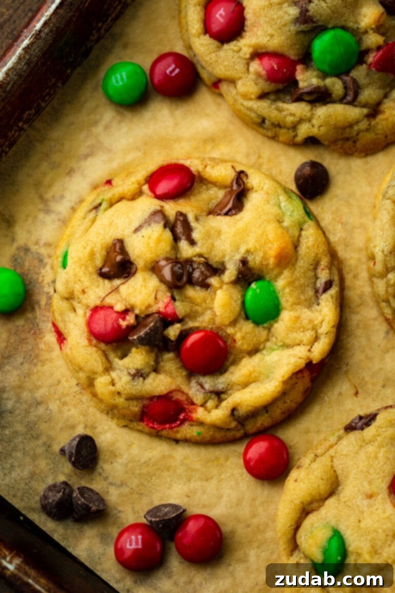 An overhead shot of a single, thick, golden-baked M&M Christmas chocolate chip cookie, showcasing its chewy texture and festive candy pieces.