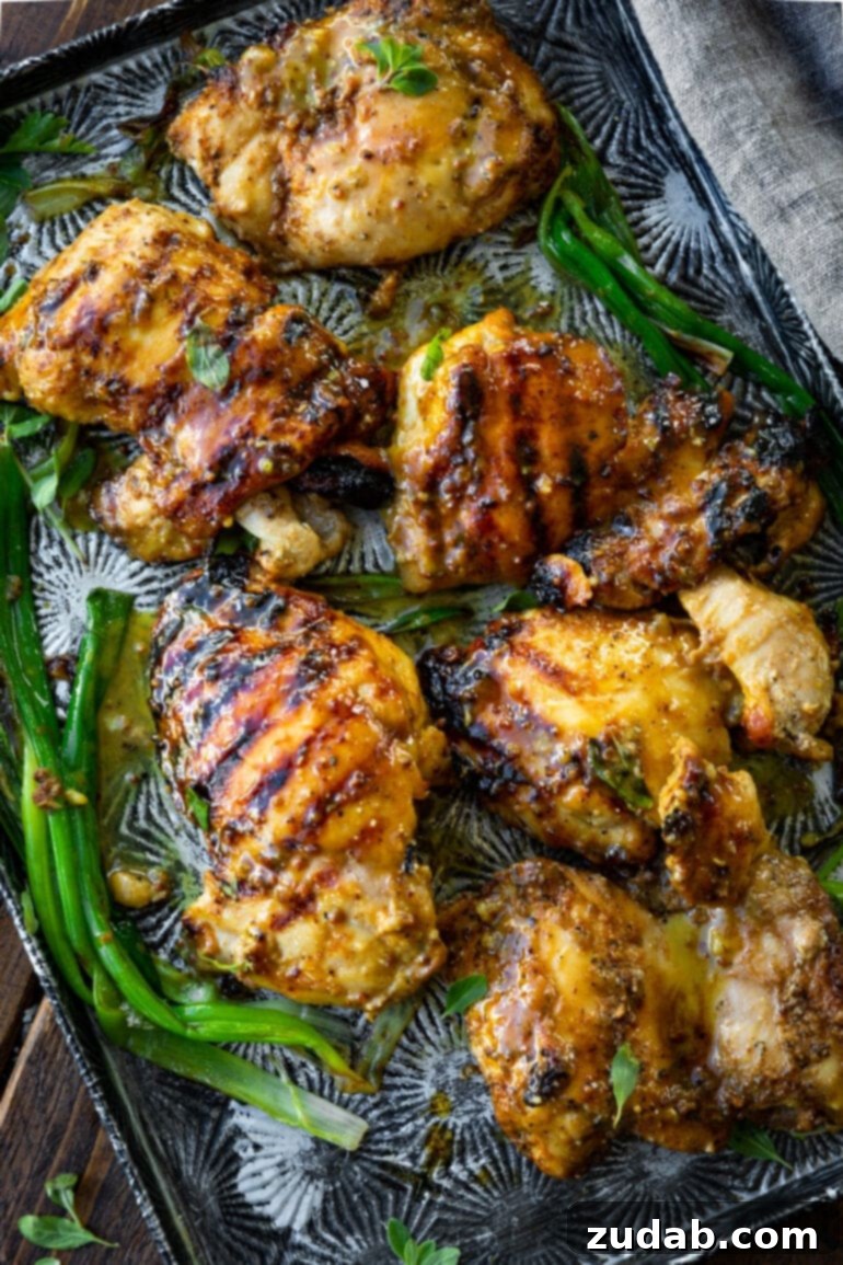Maple Mustard Glazed Grilled Chicken Thighs 3 A photo of several juicy grilled chicken thighs, beautifully glazed with a maple mustard marinade, resting on a baking sheet, ready to be served.