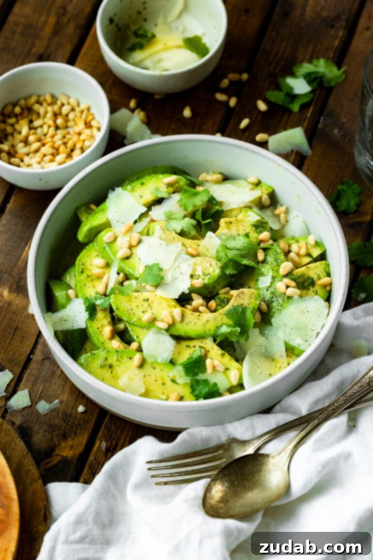 Quick Avocado Delight 3 A photo of a white serving bowl brimming with sliced avocados, mixed with toasted pine nuts, Manchego cheese, and a glossy vinaigrette dressing, capturing the salad's vibrant freshness.