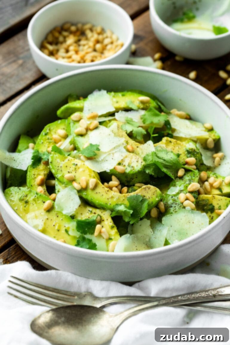 Quick Avocado Delight 6 A close-up shot of a bowl of avocado salad featuring perfectly sliced avocados, toasted pine nuts, and generous shreds of Manchego cheese, showcasing the vibrant textures and colors of the dish.